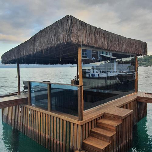 a restaurant on the water with a thatched roof at Residência Angra Deep Blue in Angra dos Reis