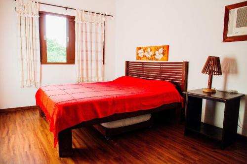 a bedroom with a red bed and a table and a window at Pousada Village Porto Mirim por Carpediem in Jacumã