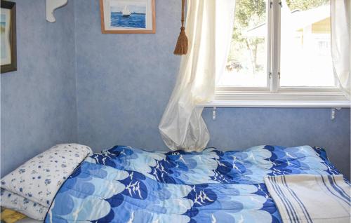 a bed with a blue and white comforter and a window at Nice Home In Kolmrden With Kitchenette in Kolmården