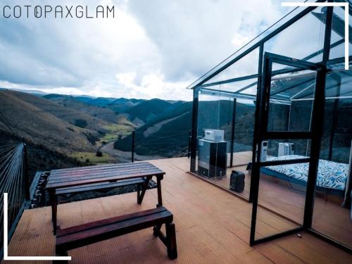 une maison en verre avec un lit et un banc sur une terrasse dans l'établissement Cotopaxglam, à Latacunga