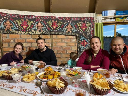 a group of people sitting at a table with food at Yurt camp Sonun in Bokonbayevo