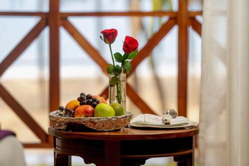 a table with a bowl of fruit and a vase with roses at Malabar Ocean Front Resort And Spa, Bekal in Nīleshwar