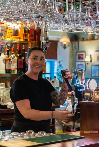 a woman standing behind a bar holding a drink at Foley's Guesthouse & Self Catering Holiday Homes in Kenmare