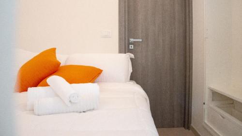 ein weißes Bett mit orangefarbenen Kissen und Handtüchern darauf in der Unterkunft Casetta La Conchiglia in Villanova di Ostuni