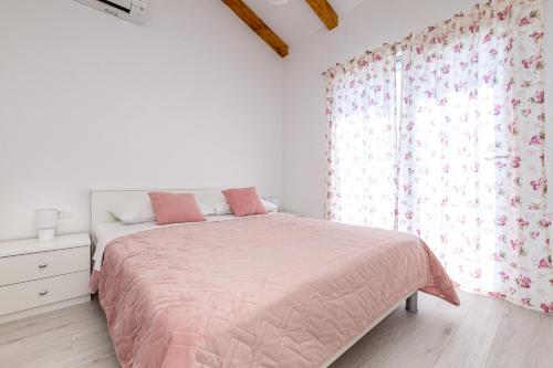 a white bedroom with a pink bed and a window at La Terza in Krk