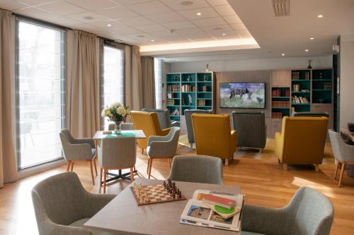 a waiting room with chairs and tables and a library at DOMITYS La SARDONNE centre-ville in Le Puy en Velay