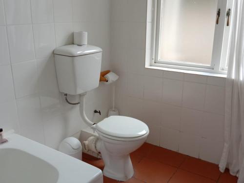 a white bathroom with a toilet and a window at Boulders Beach Hotel, Cafe and Curio shop in Simonʼs Town