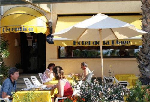 a group of people sitting at a table with an umbrella at Hotel de la Plage - Barcares in Le Barcarès