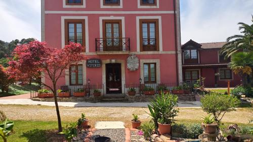 a pink building with a tree in front of it at Hotel Vitorio in Cudillero