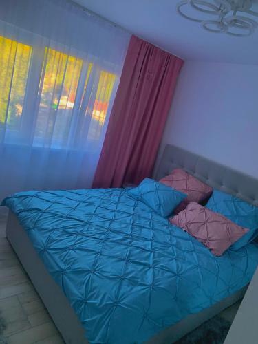 a bed with a blue comforter in a room with windows at Apartament Infinity Petroșani in Petroşani
