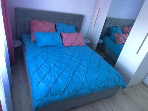 Un pequeño dormitorio con una cama azul con almohadas rosas y azules en Apartament Infinity Petroșani, en Petroşani