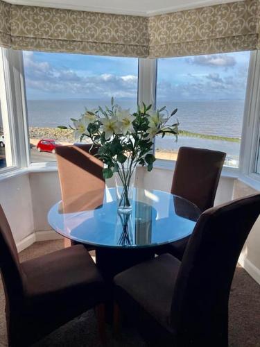 una mesa de cristal con un jarrón de flores en una ventana en fabulous sea views and sunsets, en Morecambe