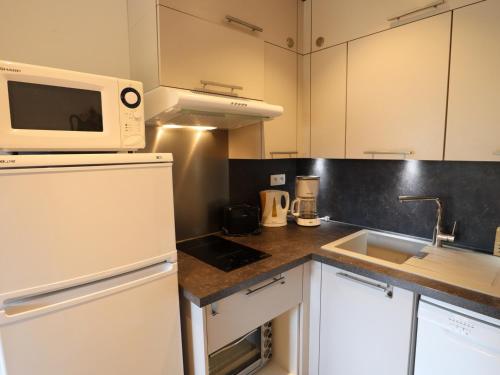 La cuisine est équipée d'un réfrigérateur blanc et d'un four micro-ondes. dans l'établissement Bel Appartement aux Gets - Proche des Pistes avec Balcon et Parking - FR-1-623-203, aux Gets
