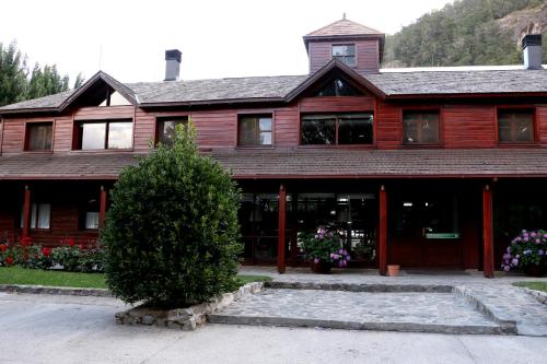 une grande maison en bois avec un arbre en face de celle-ci dans l'établissement Rincón de los Andes Resort, à San Martín de los Andes