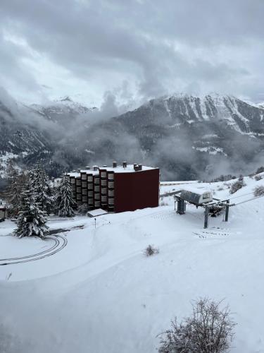 a building in the snow with mountains in the background at Très joli studio au calme et bien situé in Orcières