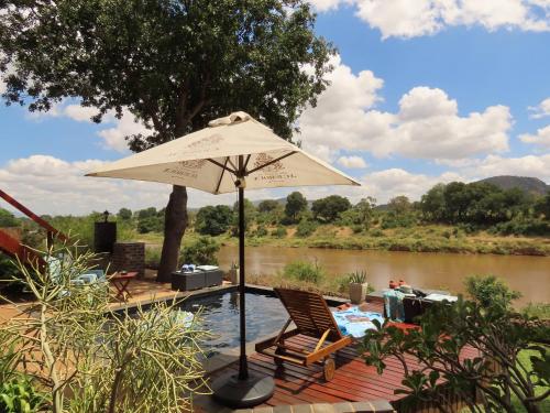 a patio with an umbrella and chairs next to a river at Hennie's Rest in Malelane