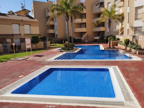 una fila di piscine blu di fronte a un edificio di The Hideaway 2 Bed Poolside Groundfloor Apartment On Albatros Full AC Free Fast Wifi a Los Alcázares