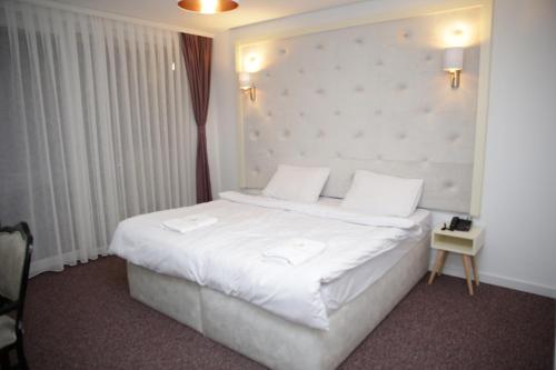 Magra Austria Hotel & Restaurant Prishtine في بريشتيني: غرفة نوم بسرير كبير عليها شراشف ووسائد بيضاء