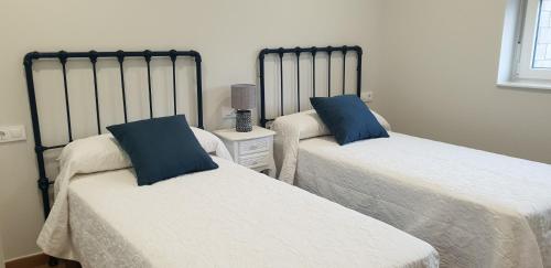 2 Betten mit blauen Kissen im Schlafzimmer in der Unterkunft A Solaina in Lariño