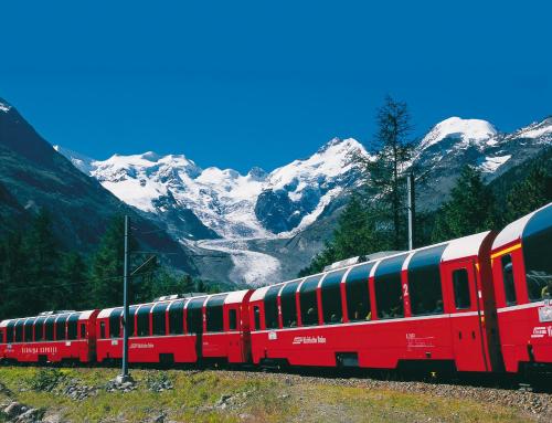 a red train is on the tracks with snow covered mountains at Hotel Sassella in Grosio