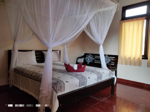 ein Schlafzimmer mit einem Himmelbett mit roten Kissen darauf in der Unterkunft Sukma Guest House in Ubud