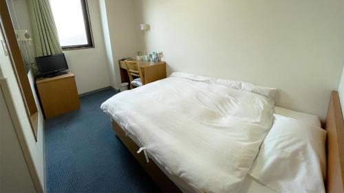 Schlafzimmer mit einem Bett mit weißer Bettwäsche und einem TV in der Unterkunft Business Hotel Rupinasu in Takamatsu