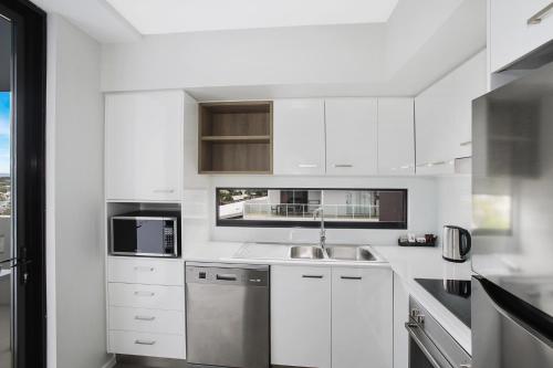 a kitchen with white cabinets and white appliances at Direct Hotels - Sea Breeze Mooloolaba in Mooloolaba