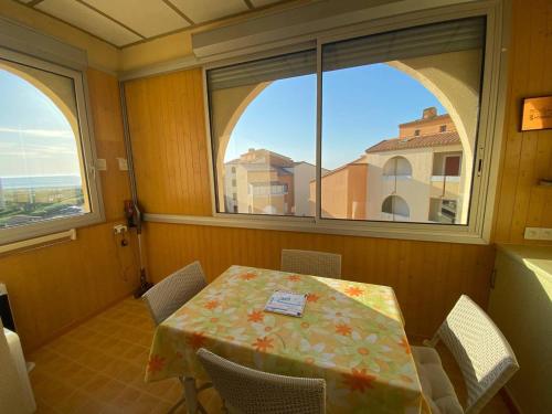 une salle à manger avec une table et deux fenêtres dans l'établissement Appartement T2+Mezzanine, 6 pers, Clim, Parking, 400m des commerces - FR-1-81-562, à Port-Leucate