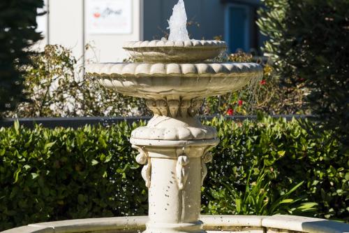 a stone fountain in a garden with bushes at Tresori Motor Lodge in Akaroa