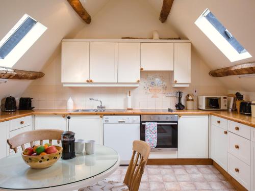 a kitchen with white cabinets and a table with a bowl of fruit at Hayloft at NewBarn Farm in Chipping Norton