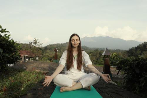 a woman sitting on a yoga mat with mountains in the background at Jeevess Retreat Wayanad in Wayanad
