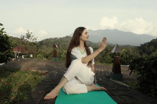 a woman is sitting on a green yoga mat at Jeevess Retreat Wayanad in Wayanad