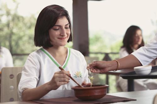 a woman sitting at a table eating a bowl of food at Jeevess Retreat Wayanad in Wayanad