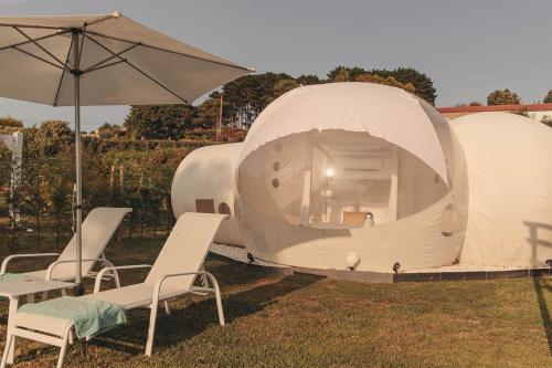 Tienda de campaña blanca grande con sillas y sombrilla en Burbujas Astronómicas Albarari Coruña, en Oleiros