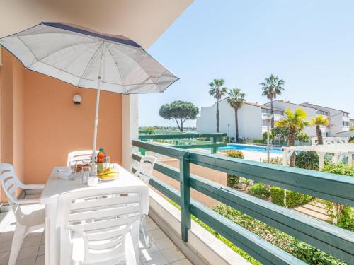 un balcon avec une table, des chaises et un parasol dans l'établissement Apartment Les Terrasses du Lac-7 by Interhome, au Grau-du-Roi