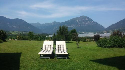 two white chairs in a field with mountains in the background at Casa Vacanze Hartriegel in Comano Terme