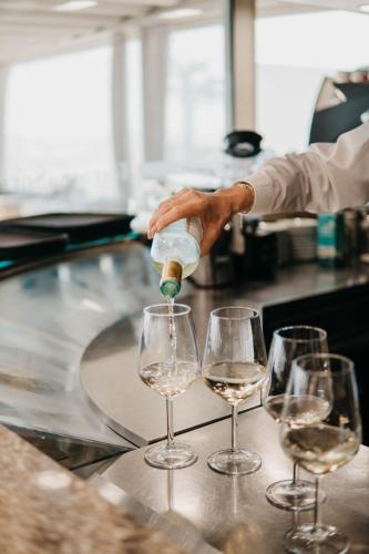 a person pouring white wine into three wine glasses at Hotel Villa Sorriso in Lido di Jesolo