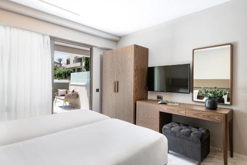 a bedroom with a bed and a desk with a television at Porto Platanias Beach Luxury Selection - Adults Only in Plataniás