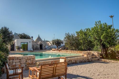 a swimming pool with two wooden benches next to a house at Trullo La Succulenta in Ceglie Messapica