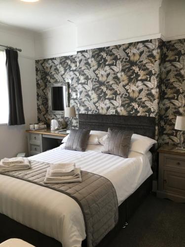 1 dormitorio con 1 cama grande y papel pintado con motivos florales en The Kenmore Guest House en Llandudno