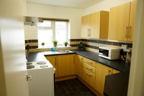 a kitchen with wooden cabinets and a sink and a microwave at 10BH Dreams Unlimited- Budget Heathrow Long stay Apartment with FREE PARKING in Ashford