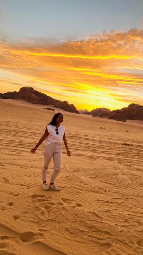 a woman standing in the desert with the sunset in the background at Rum Jordan camp and tours in Wadi Rum