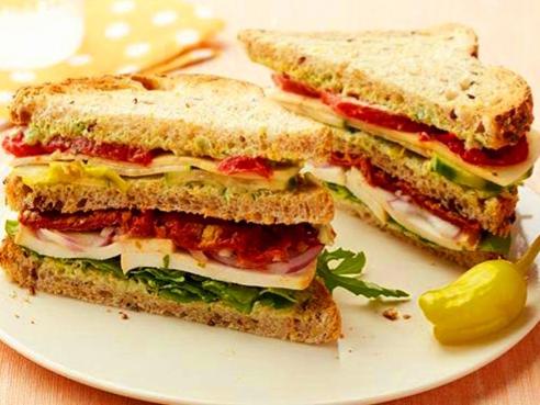 a sandwich cut in half on a plate with a pickle at Hotel Merriment Alpha in Noida