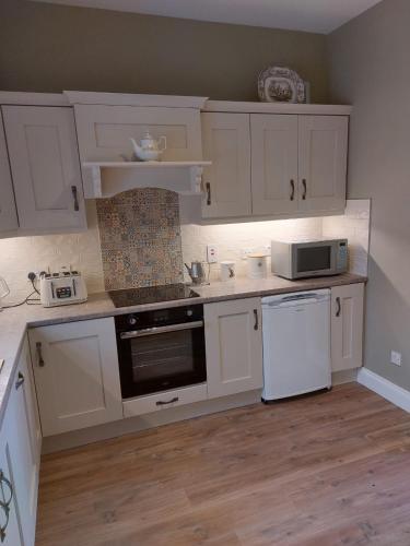 a kitchen with white cabinets and a stove and a microwave at Drumlaghy House in Florencecourt