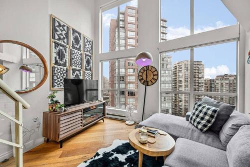 a living room with a couch and a tv and windows at Beautiful Downtown Loft with full kitchen in Vancouver