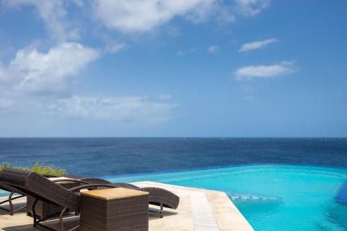 a pool with chairs and the ocean in the background at Cliff Villa - Award Winning Luxury Retreat in Westpunt