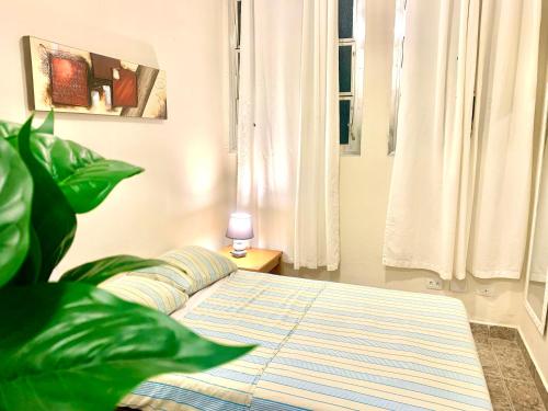 Un dormitorio con una cama y una planta y una ventana. en Suíte 300 Pitangueiras - na quadra da praia, en Guarujá