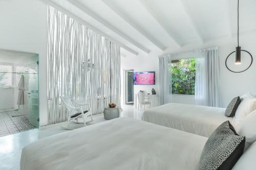 a white bedroom with two beds and a bathroom at Gigi Brown Beachfront Santa Teresa in Santa Teresa Beach