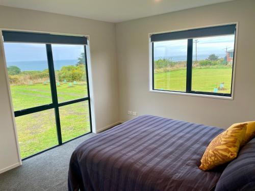 a bedroom with a bed and two large windows at Toko Mouth Beach House in Glenledi