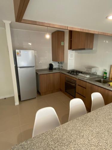 a kitchen with a white refrigerator and wooden cabinets at Hermoso y Tranquilo Departamento / Parquemar 3 in El Tabo